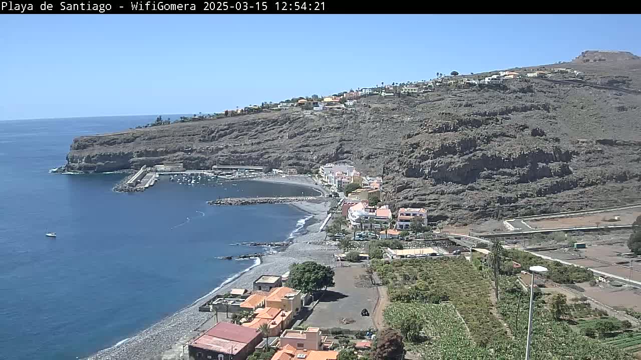 A coastal town nestled against a rocky hillside overlooking a calm ocean, under a clear blue sky.