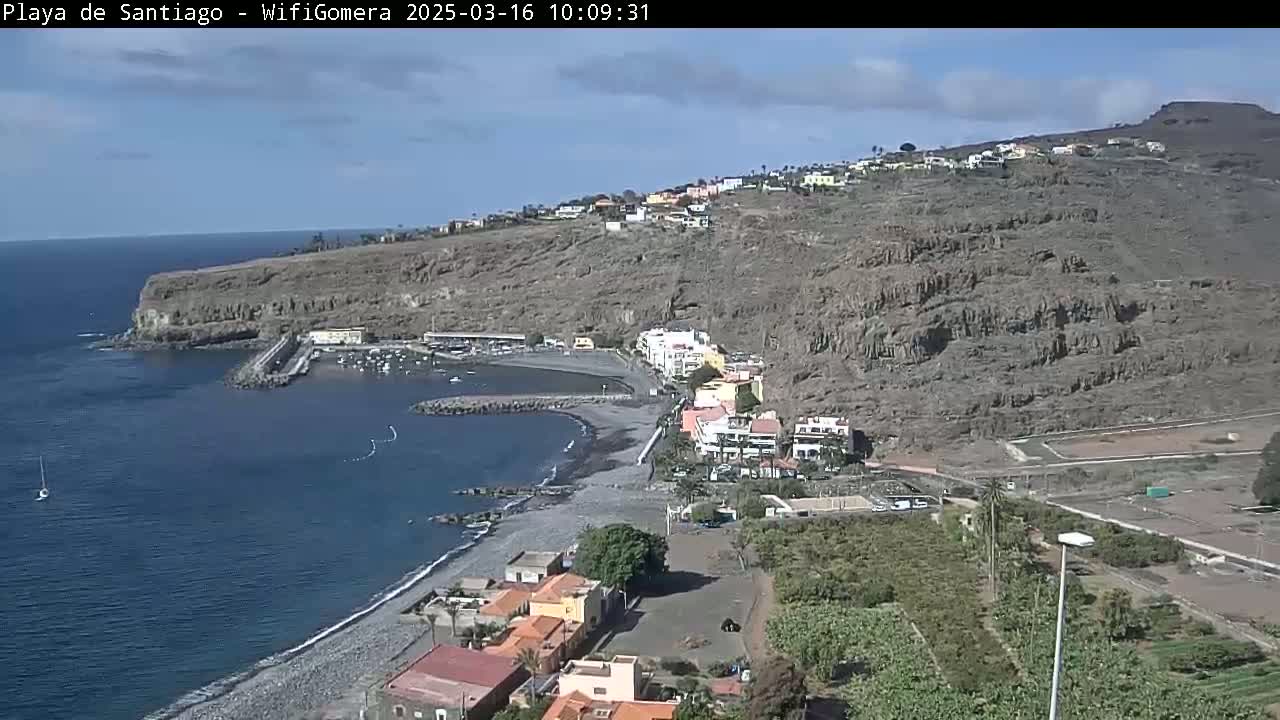 A coastal town with a small harbor nestled against a steep, rocky hillside under a mostly clear sky.