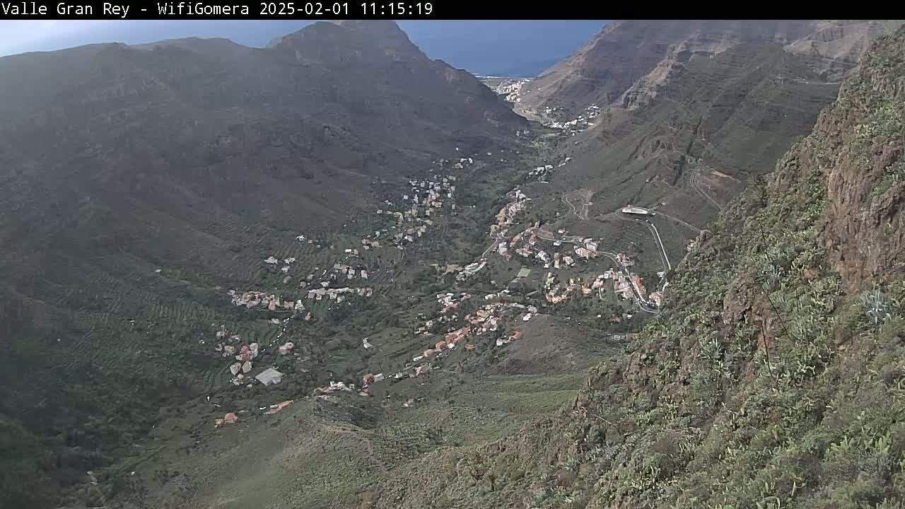 A mountainous valley town is visible from an elevated vantage point on a partly cloudy day.