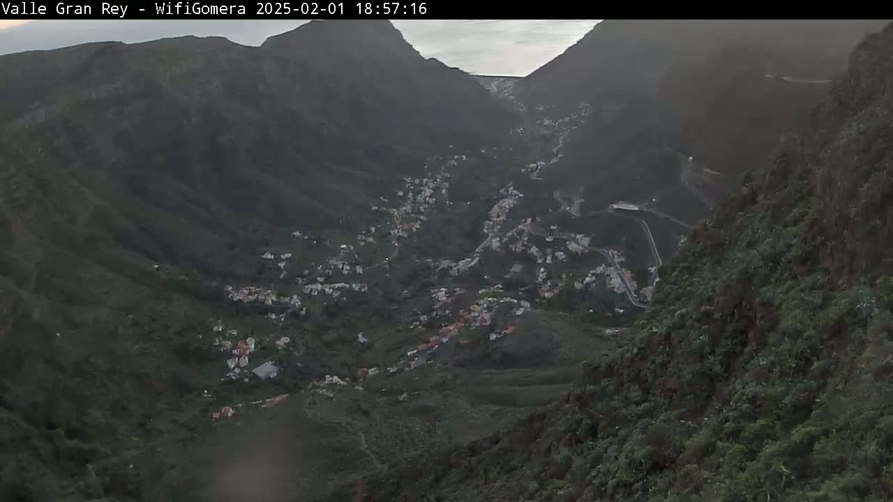 A mountain valley town nestled between steep, dark green hillsides under a mostly cloudy, dusky sky.