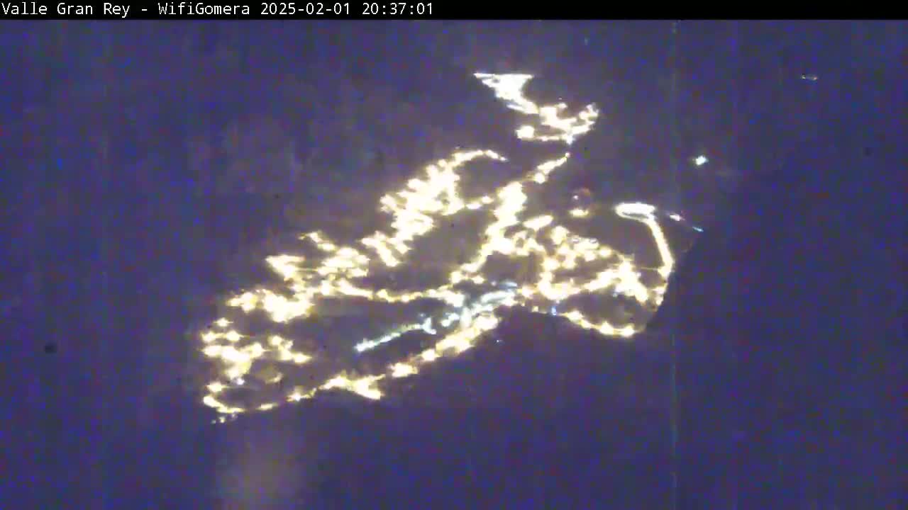 A nighttime, long-range view shows the lights of a city or town spread across a dark landscape.