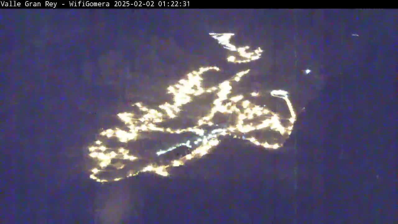 A nighttime view shows a city's lights scattered across a dark landscape.