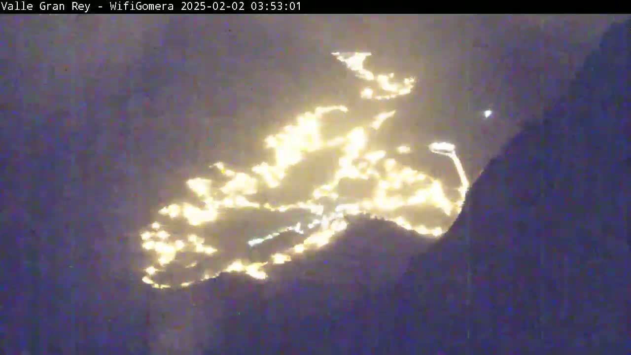 A nighttime long shot shows a collection of lights illuminating the side of a dark mountain.
