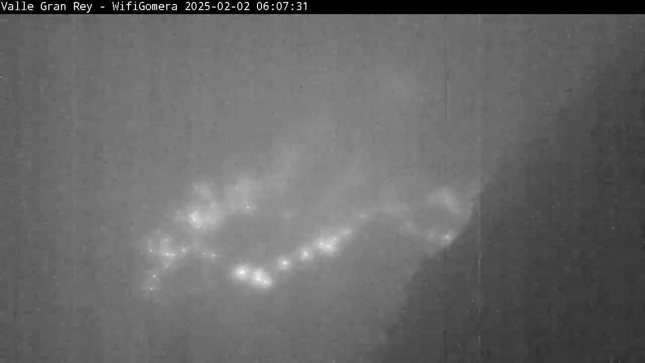 A nighttime, low-light image shows a diffuse, somewhat linear pattern of bright lights in a hazy or cloudy sky.