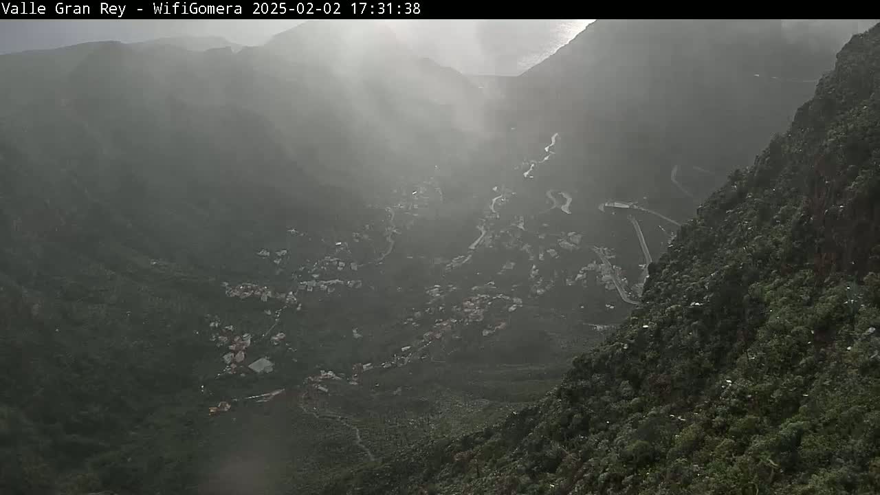 A misty, mountainous landscape reveals a winding road snaking through a village nestled in a valley.