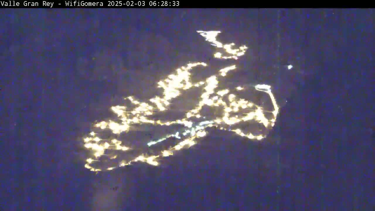 A nighttime aerial view shows the lights of a town or city scattered across a dark landscape.