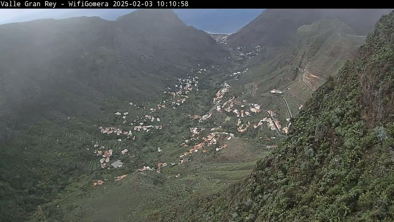 A mountainous valley town is seen from a high vantage point on a partly cloudy day.