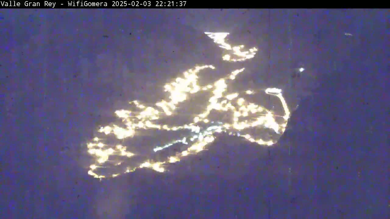 A nighttime long shot shows a hillside illuminated by scattered lights, possibly a town or village, under a dark, clear sky.