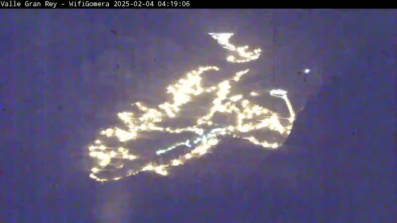 A nighttime aerial view shows a town's lights scattered across a dark landscape.