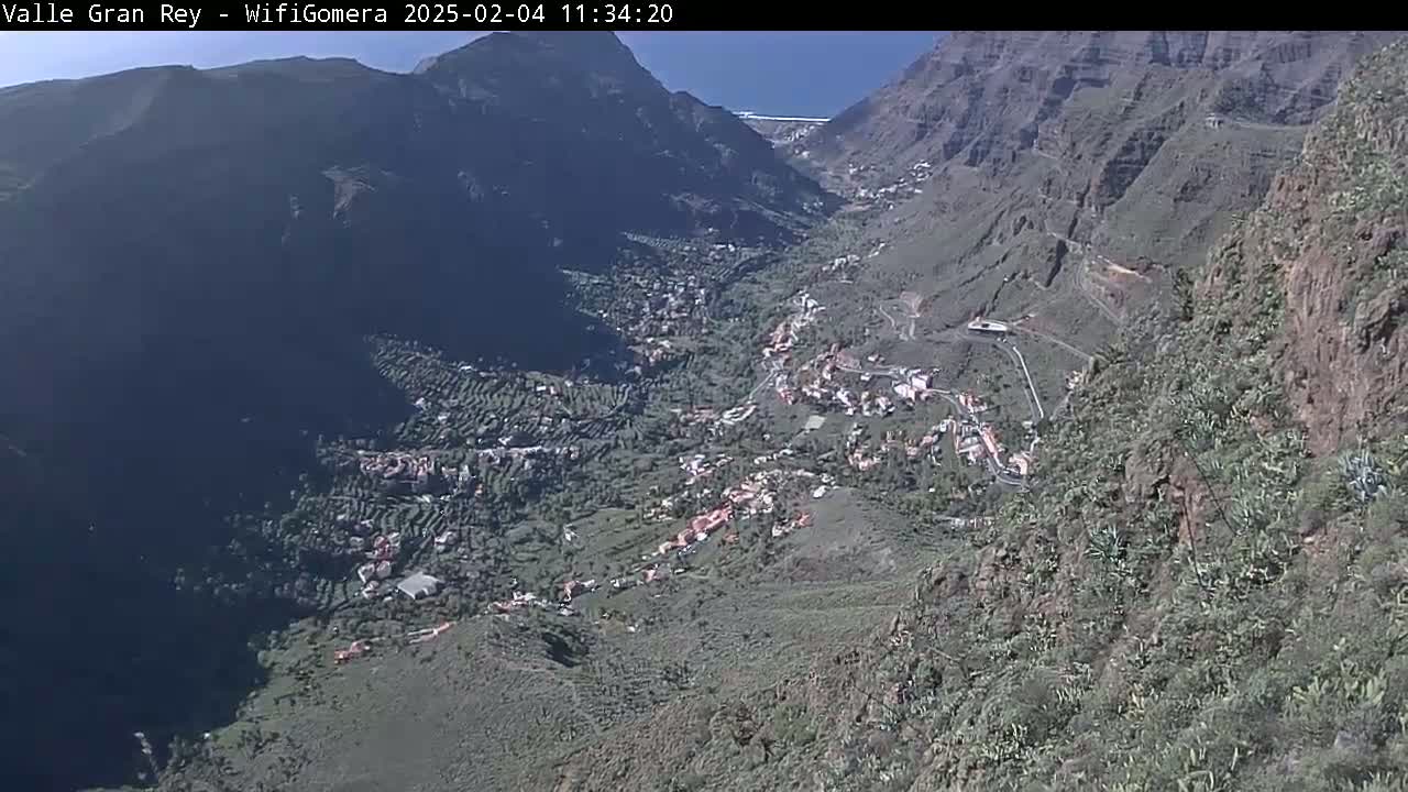 A high-angle view on a sunny day shows a town nestled in a steep, rocky valley.