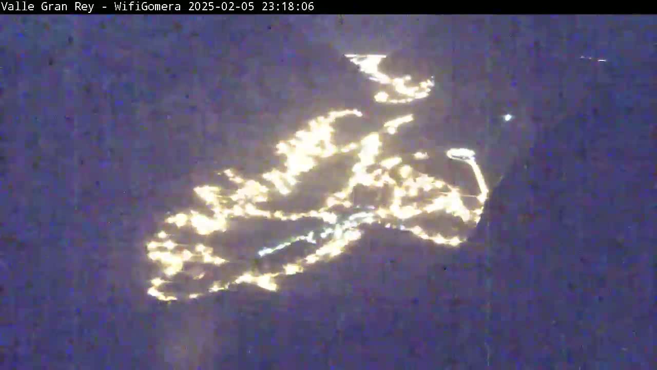 A nighttime aerial view shows a scattering of yellow-white lights spread across a dark, possibly mountainous, landscape.