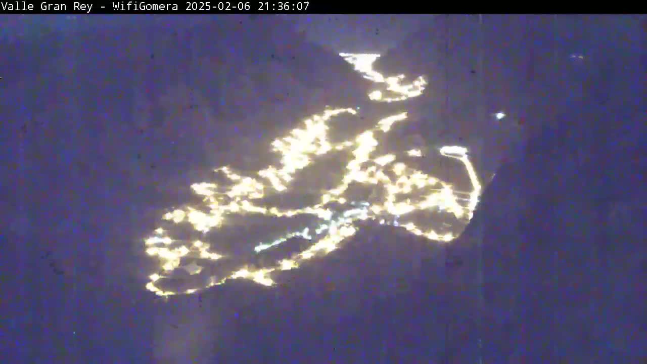 A nighttime, long-distance view shows a town's lights scattered across a dark landscape.