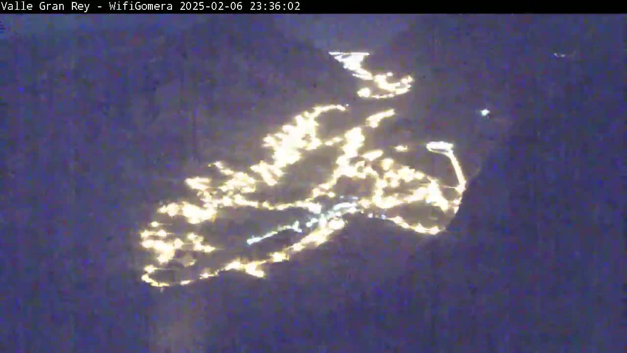 A nighttime aerial view shows a town's lights spread across a valley.