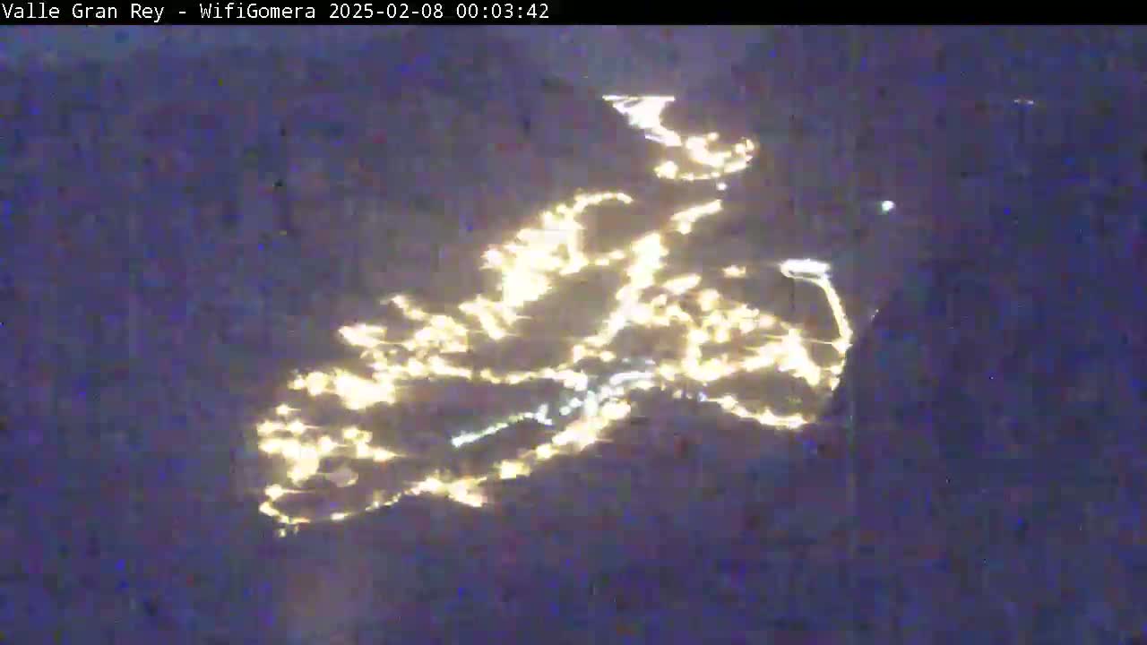 A nighttime image shows a body of water reflecting many lights from a distant city or town.