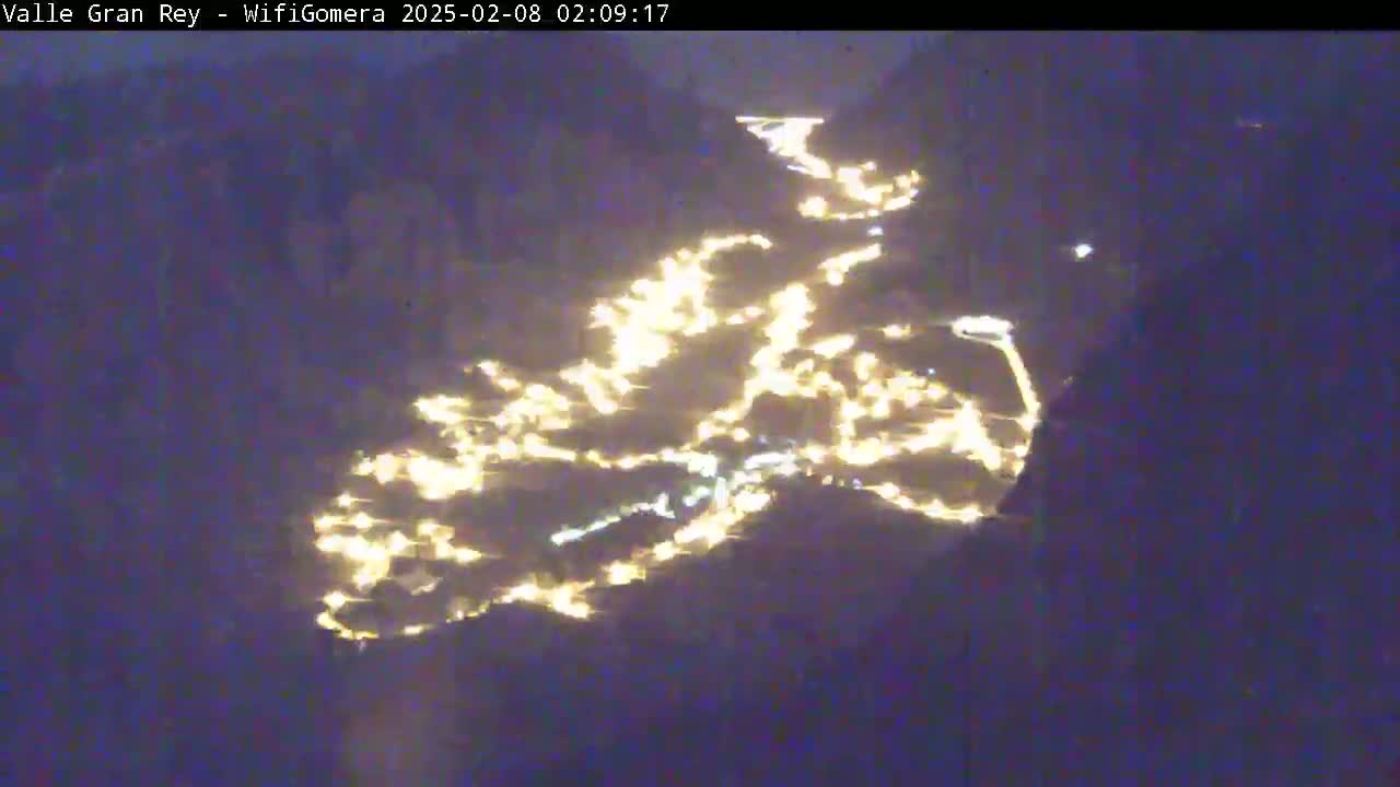 A nighttime aerial view shows a town illuminated by many lights nestled in a dark valley.