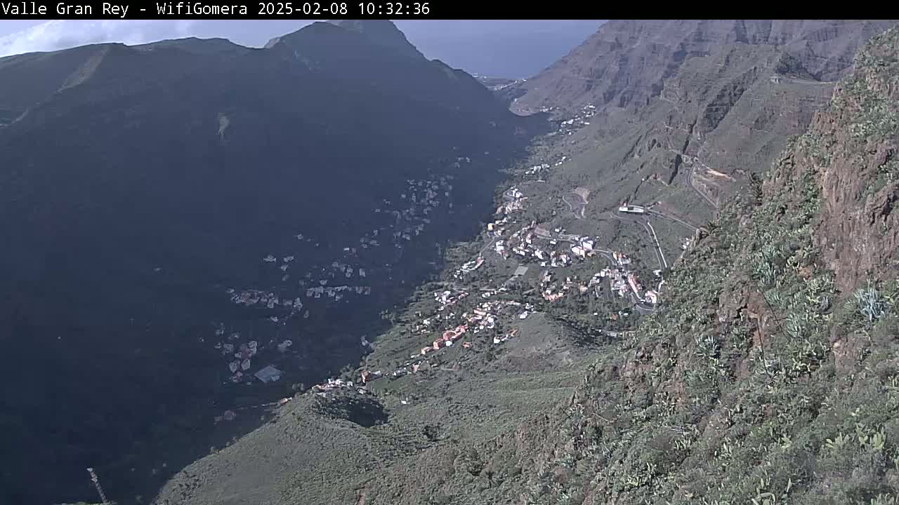 A mostly sunny day reveals a high-angle view of a town nestled in a steep, rocky valley.