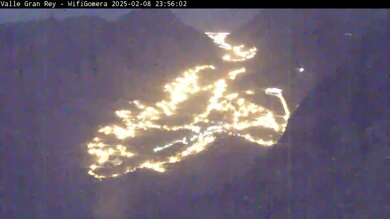 A nighttime, aerial view shows a valley illuminated by scattered lights winding through dark, mountainous terrain.