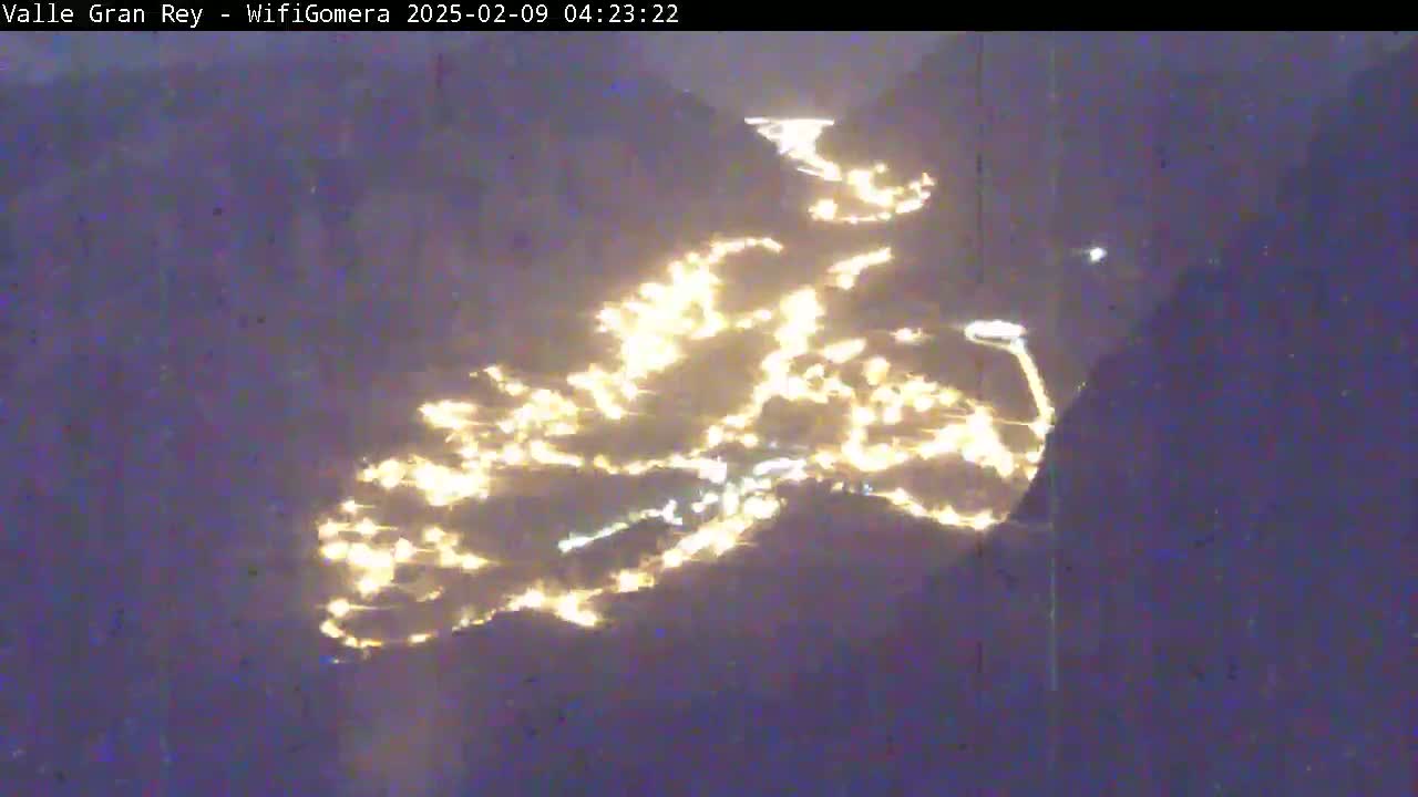 A nighttime, aerial view shows a town's lights scattered across a dark hillside.