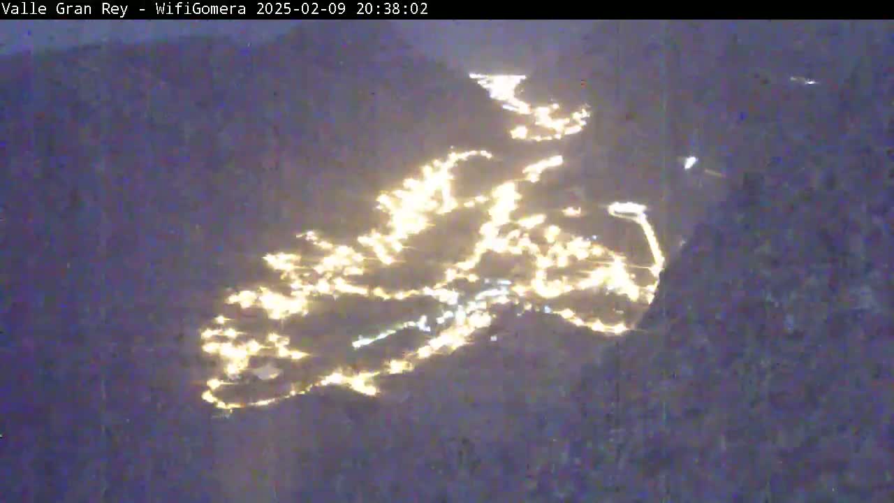 A nighttime view shows a valley town's lights scattered across a dark, mountainous landscape.