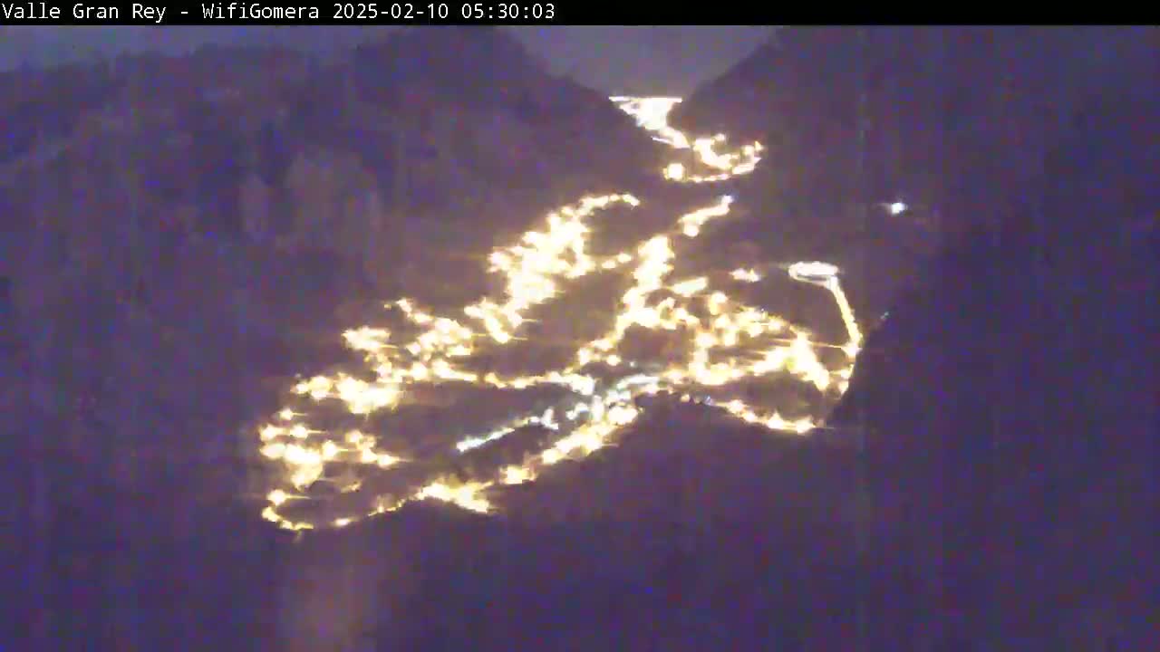 A nighttime, aerial view shows a valley illuminated by many scattered lights winding along a dark, mountainous landscape.