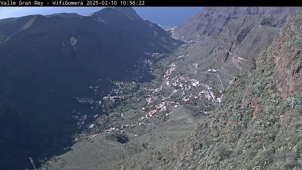 A high-angle view on a sunny day shows a small town nestled in a steep, rocky valley.