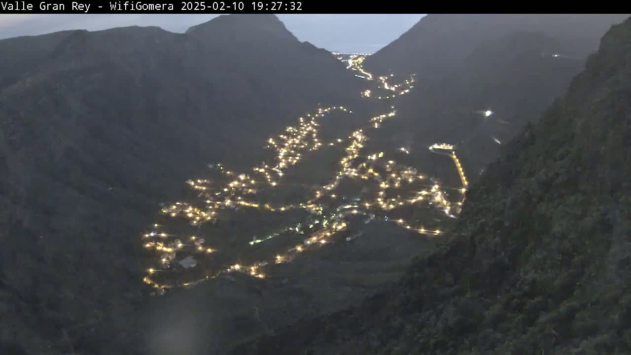 A valley nestled between dark mountains at night is illuminated by the lights of a town spread along a winding road.