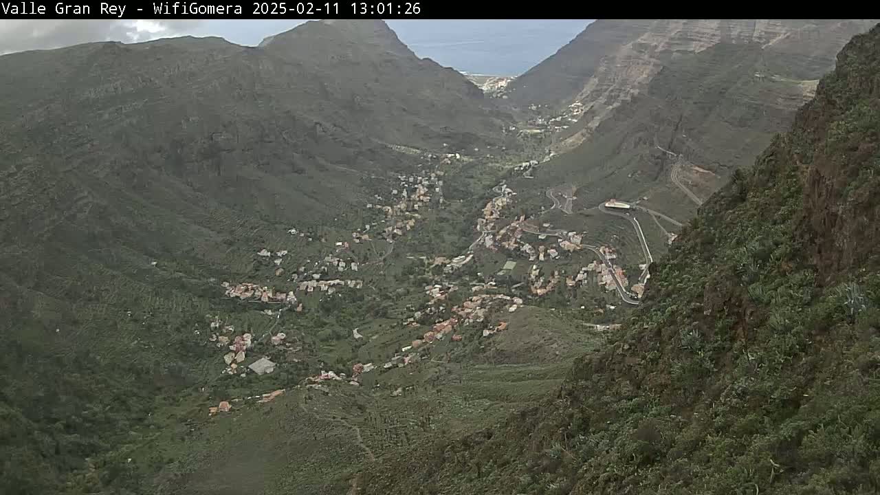 A mountainous valley town is visible from a high vantage point, under overcast skies.