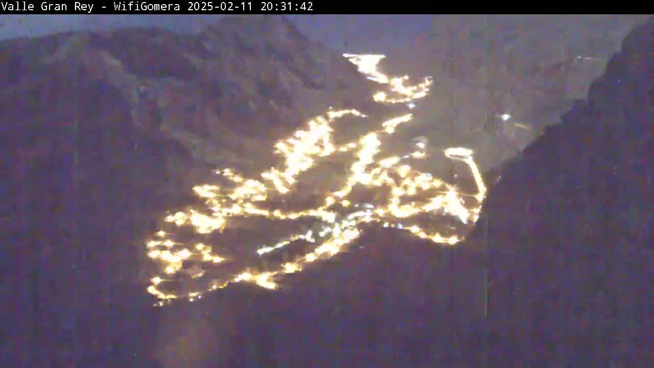 A nighttime, high-angle view shows a valley illuminated by numerous lights from a town nestled between dark mountains.