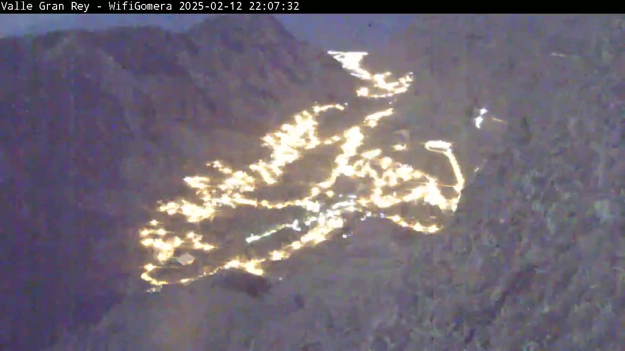 A nighttime aerial view shows a valley town illuminated by many scattered lights.