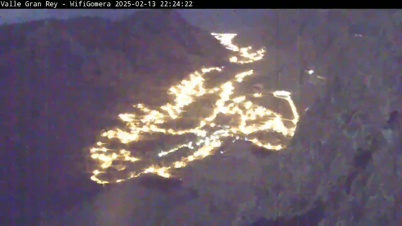 A nighttime, possibly snowy, aerial view shows a town illuminated by many scattered lights nestled in a valley.