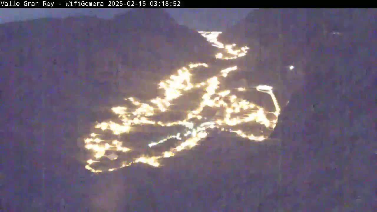 A nighttime, aerial view shows a town nestled in a valley, its lights illuminating the landscape.