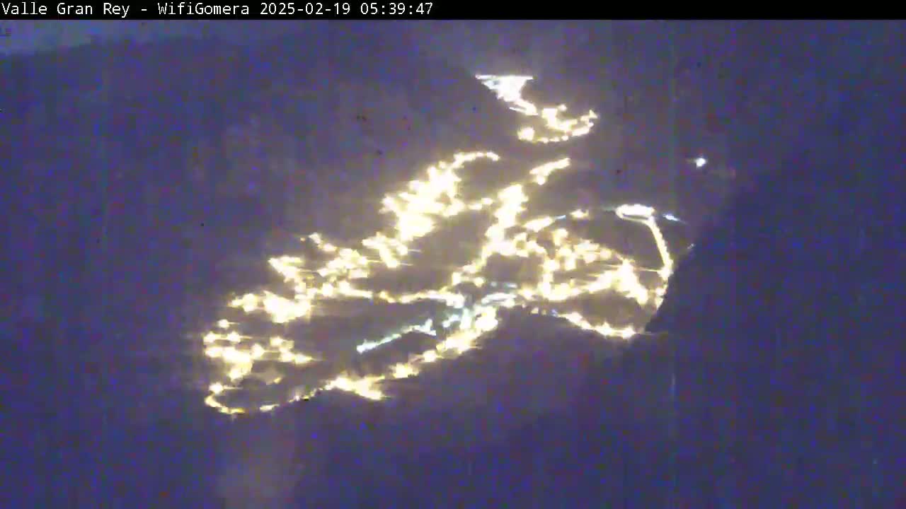 A nighttime aerial view shows a scattering of lights across a dark, possibly mountainous, landscape.