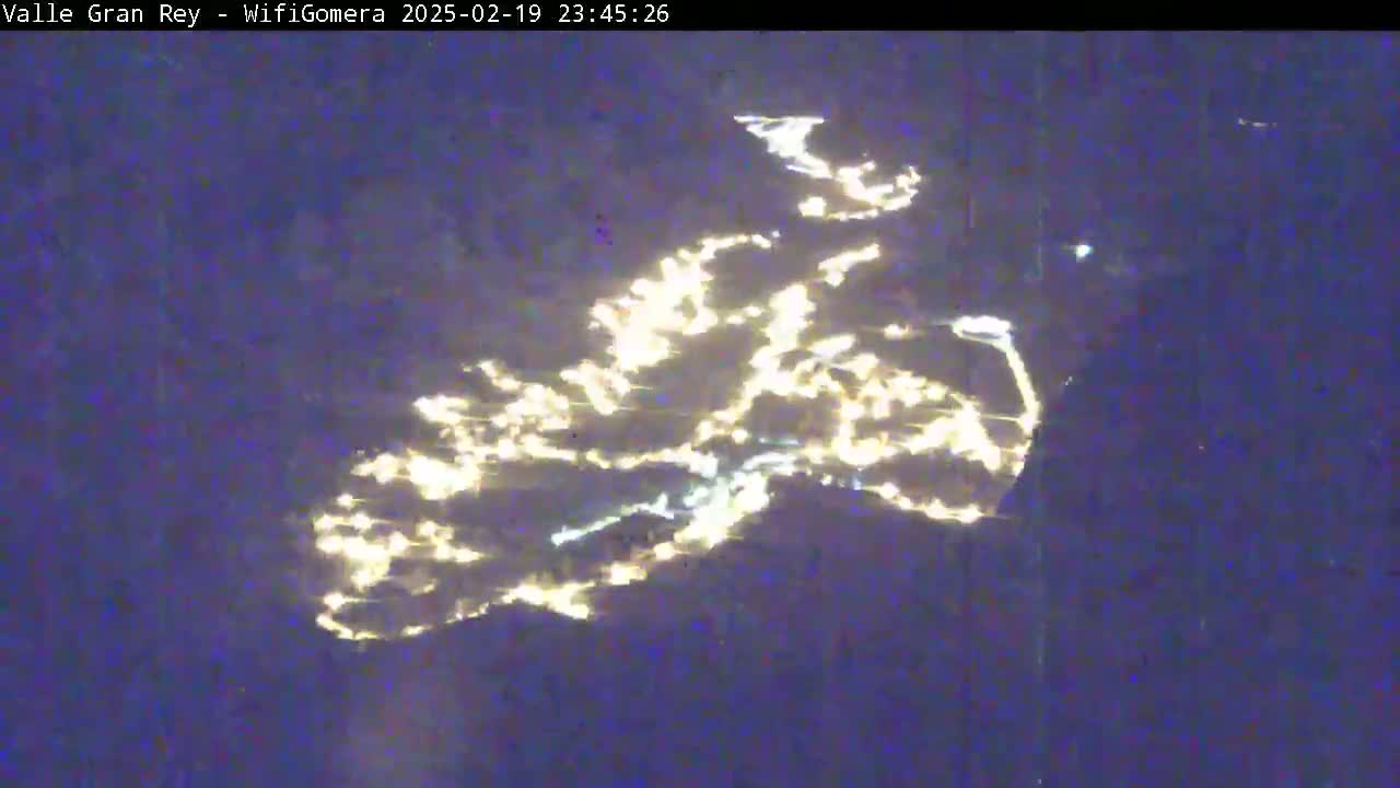 A nighttime, long-range view shows the lights of a town reflecting on a dark body of water.