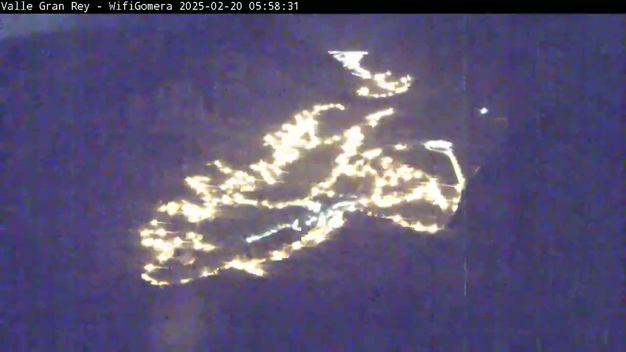An aerial nighttime view shows city lights reflecting on a dark body of water.