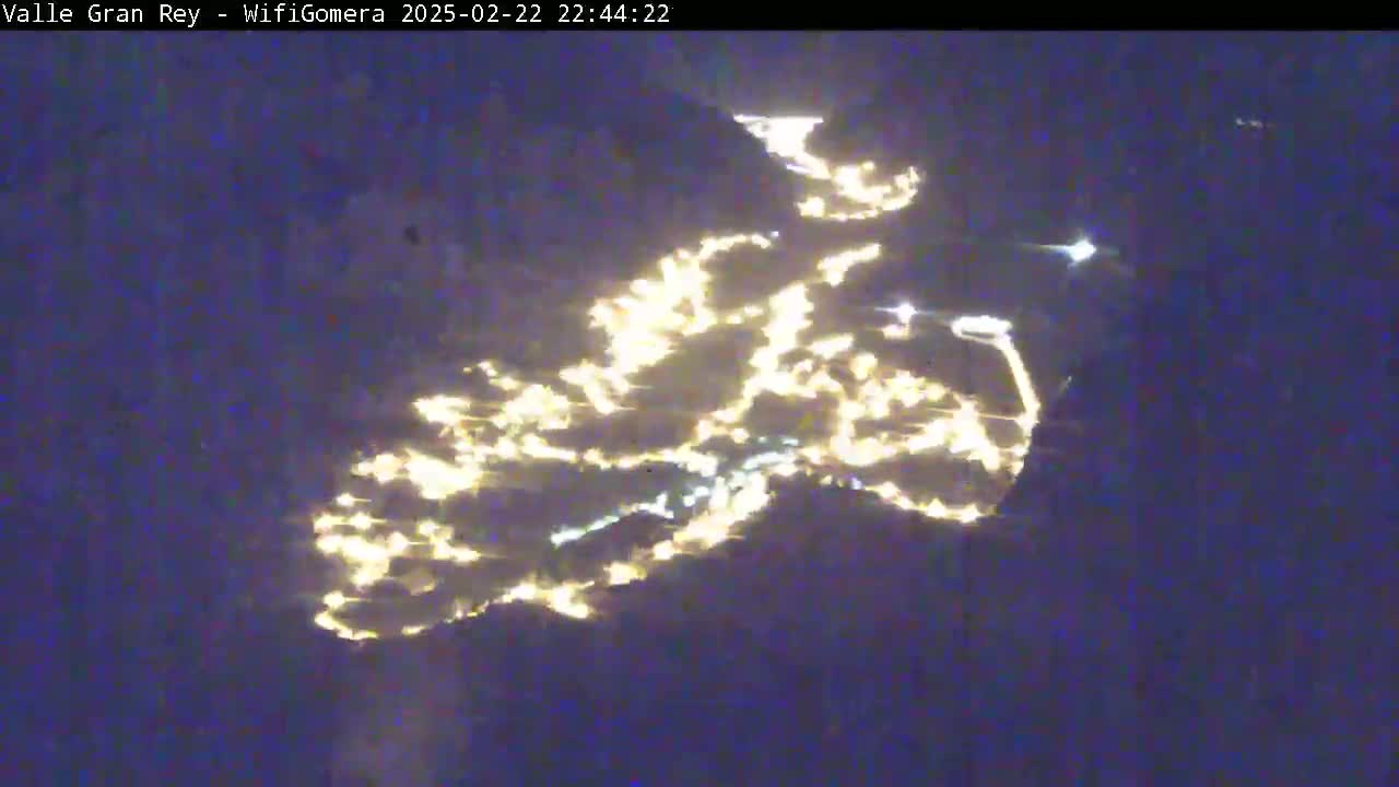 A nighttime aerial view shows a valley illuminated by many scattered lights.