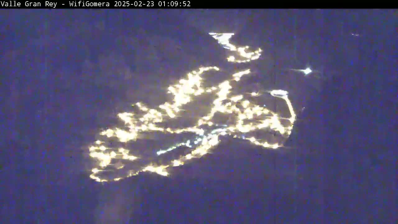 A nighttime aerial view shows a collection of lights spread across a dark landscape.