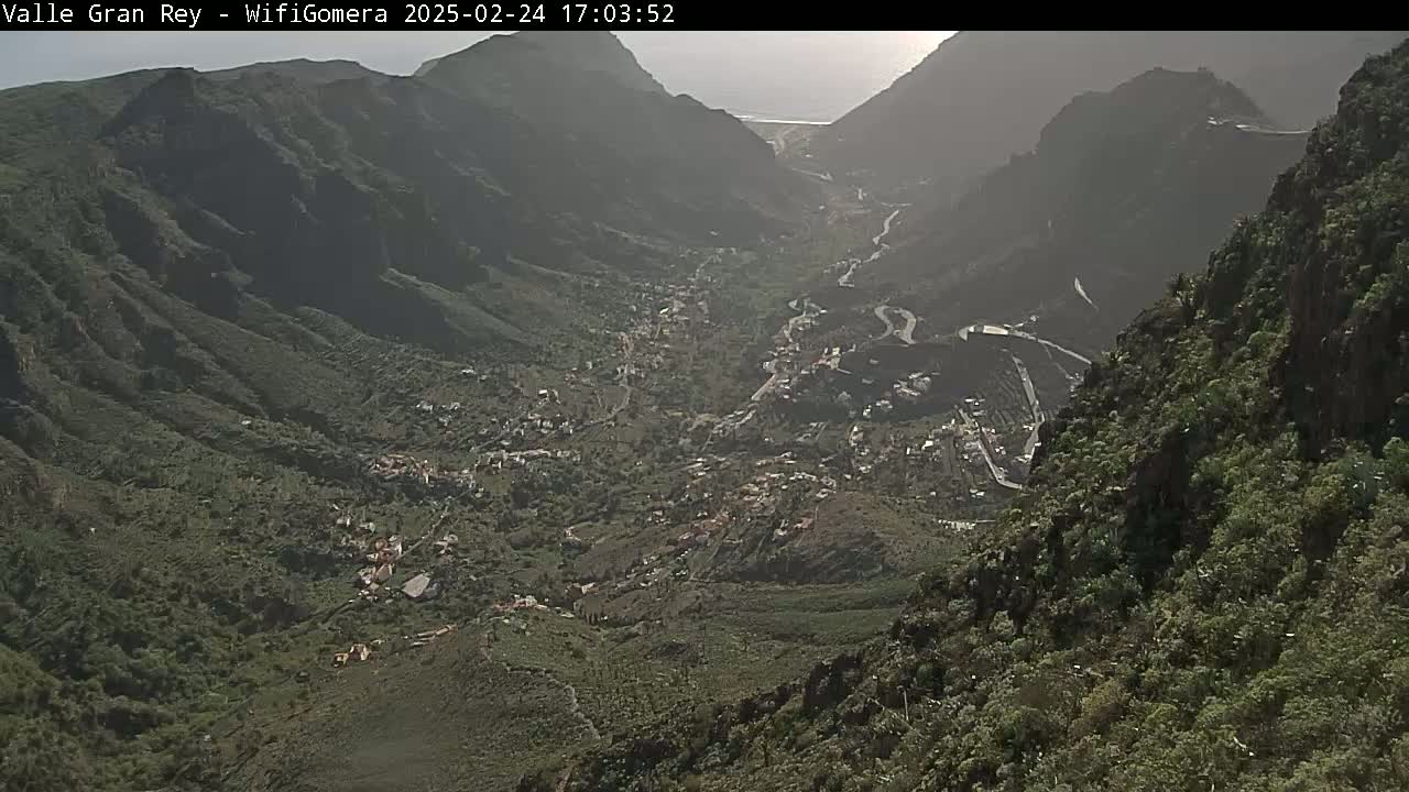 A hazy view from a mountaintop shows a valley town nestled between steep, verdant slopes.