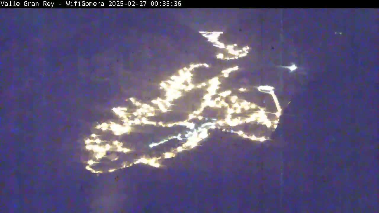A nighttime aerial view shows a scattering of yellow lights across a dark, possibly water, surface.