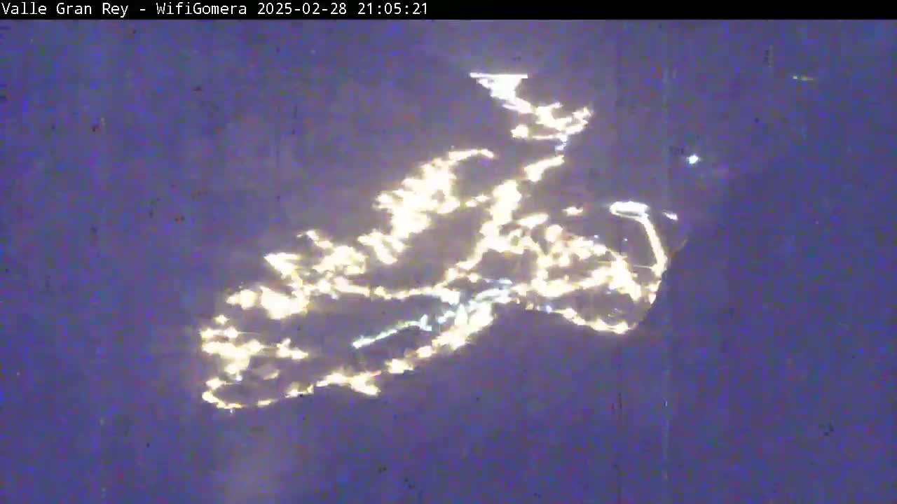 A nighttime view shows a body of water reflecting many lights from a distant town or city.