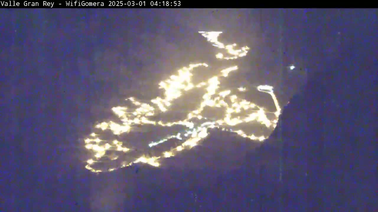 A nighttime view shows the lights of a town or city reflected on the surface of water.