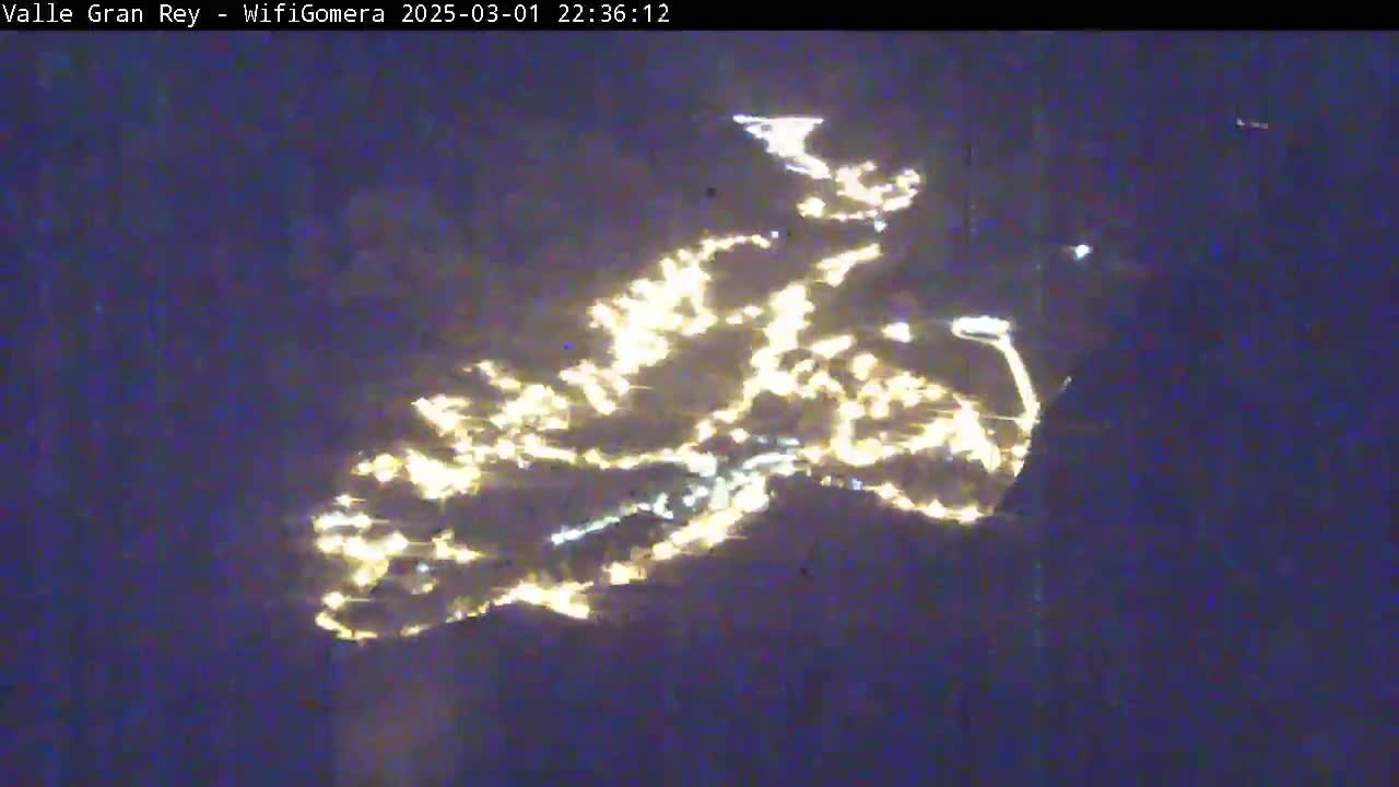 A nighttime long-range view shows the lights of a city or town spread across a dark landscape.