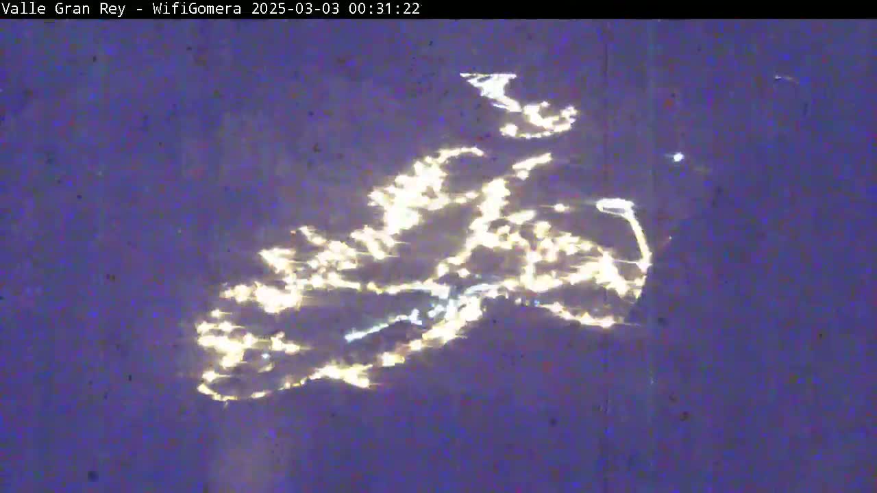 Reflected city lights shimmer on a dark body of water at night.