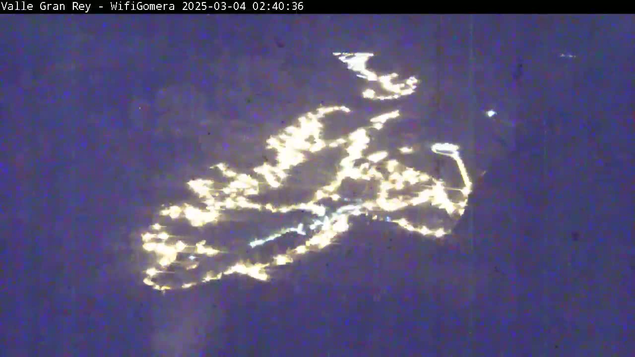 A nighttime, long-distance view shows city lights reflected on a dark body of water.
