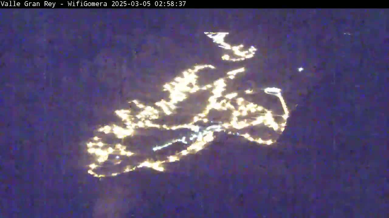 An aerial nighttime view shows a town's lights scattered across a dark landscape.