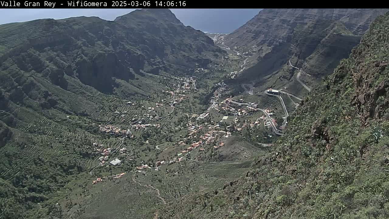 A high-angle view shows a village nestled in a mountainous valley on a sunny day.