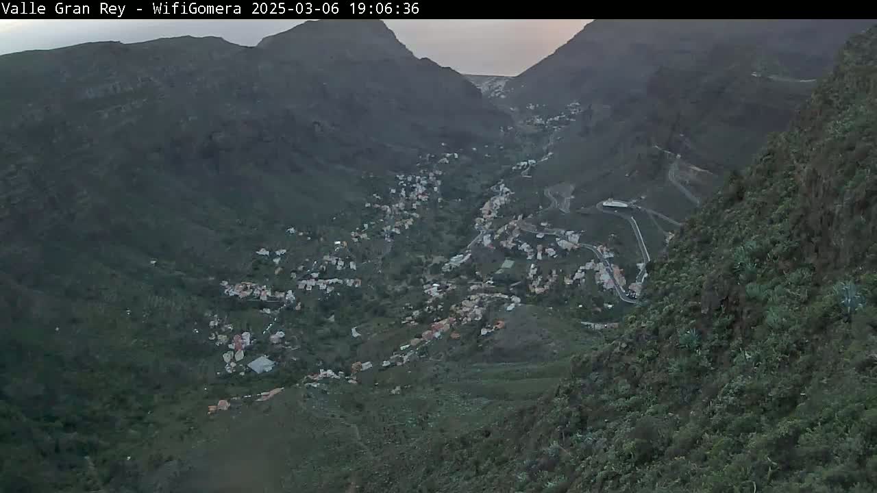 A high-angle view shows a valley nestled between mountains, containing a small town under a dusky sky.