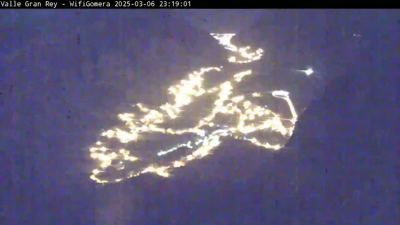 A nighttime view shows the lights of a town or city spread across a dark landscape.