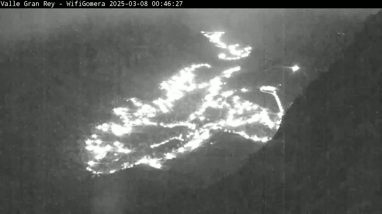 A nighttime image shows a large wildfire burning across a mountainous landscape.