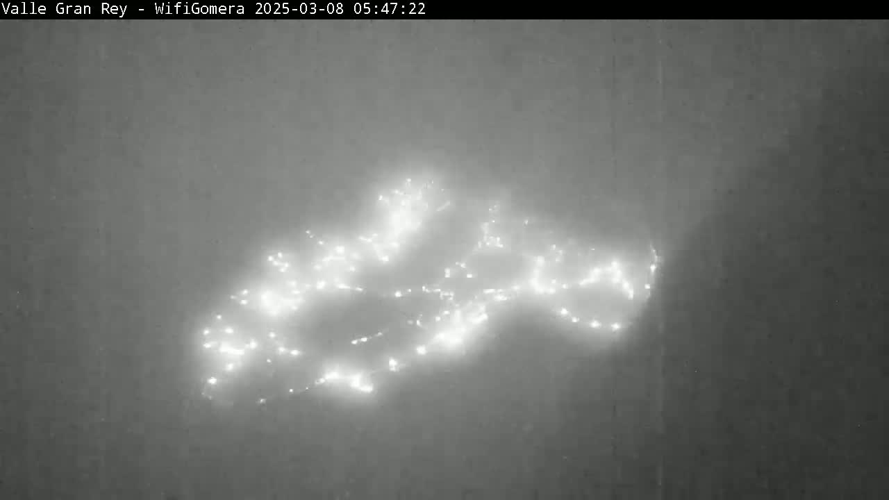 A hazy, nighttime view shows a cluster of bright lights, possibly a town or city, in the distance.