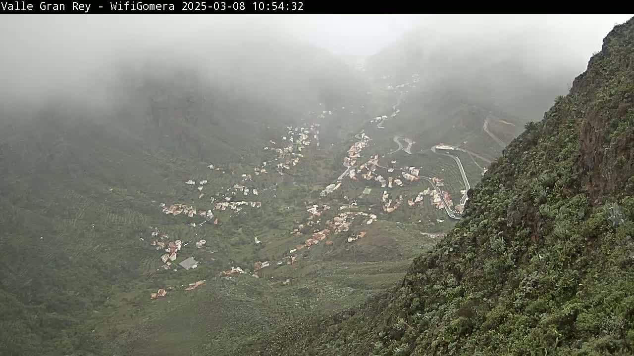 A foggy mountain valley reveals a small town nestled among verdant hills and winding roads.